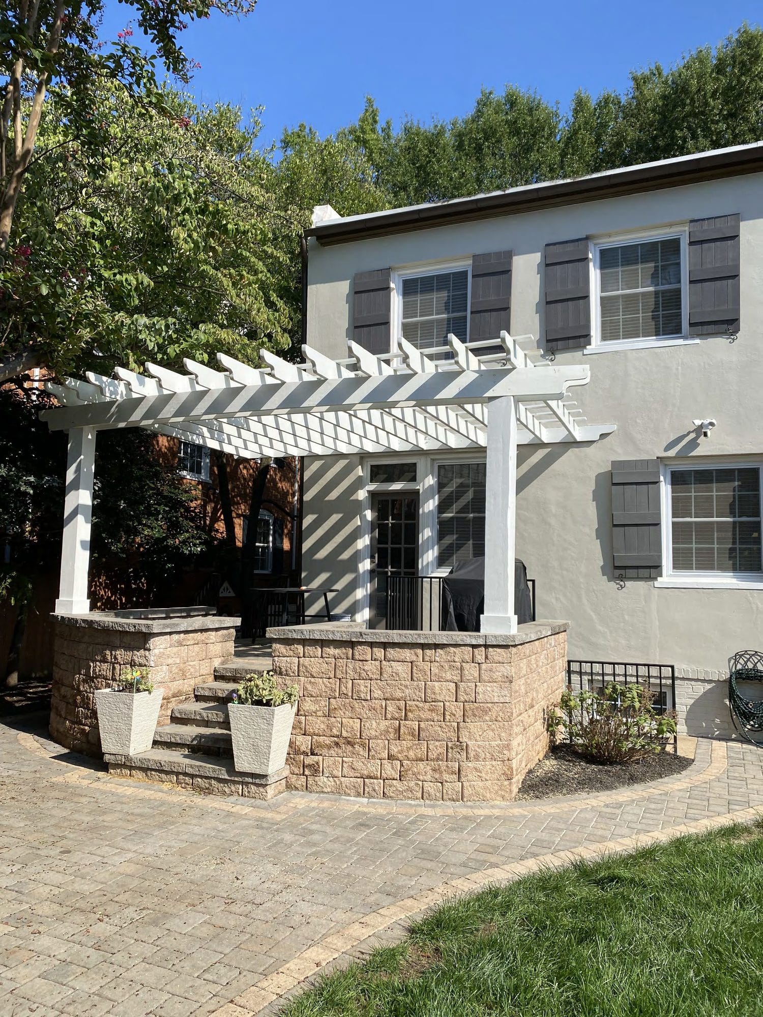 Snow blankets the yard beneath a white pergola built along the roofline of this stucco home.