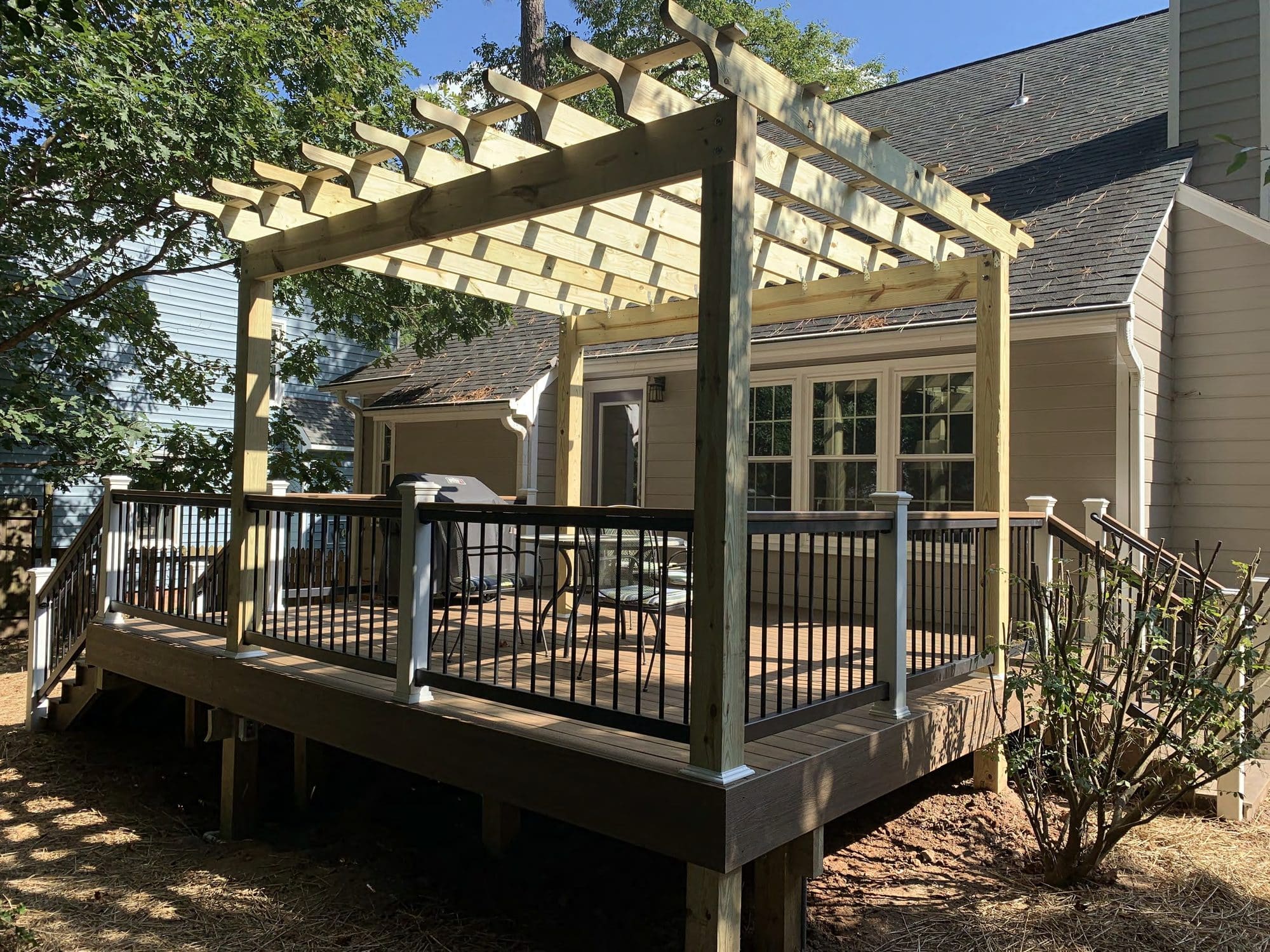 A wood pergola extends off a composite deck with black aluminum railings and a built-in grill station.